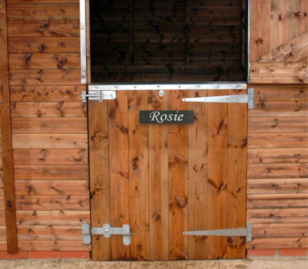 A sturdy stable wooden door with a prominently displayed stable horse sign, indicating its purpose or providing information of a horse name to a passersby.